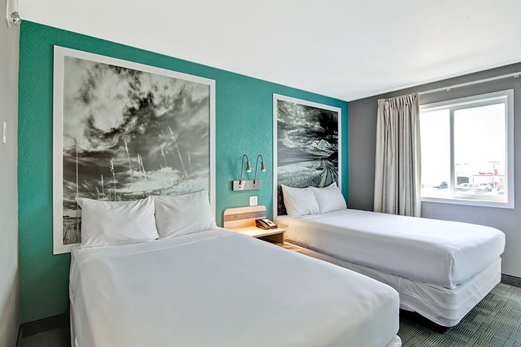 A two bed suite at d3h Home Inn Express Medicine Hat features two large framed black and white photos hanging against turquoise green walls with a large window letting in bright natural light into the room.