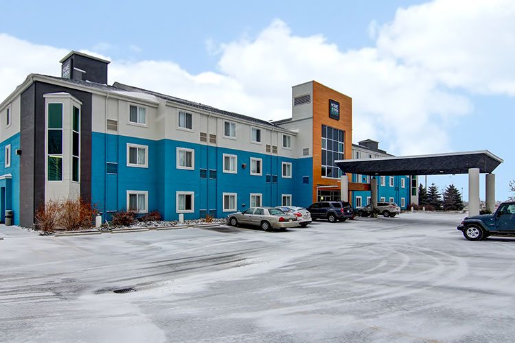 The parking lot of d3h Home Inn Express in Medicine Hat is covered with a dusting of snow with a view of the three storey hotel, painted alternately in blue, orange and white colors.