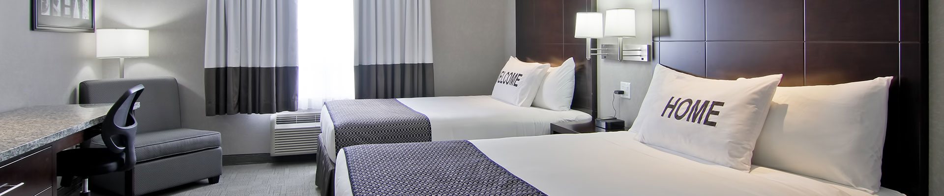 A two bed suite at d3h Home Inn & Suites Regina Airport showcases beds immaculately made up in white linen  with prominently displayed 