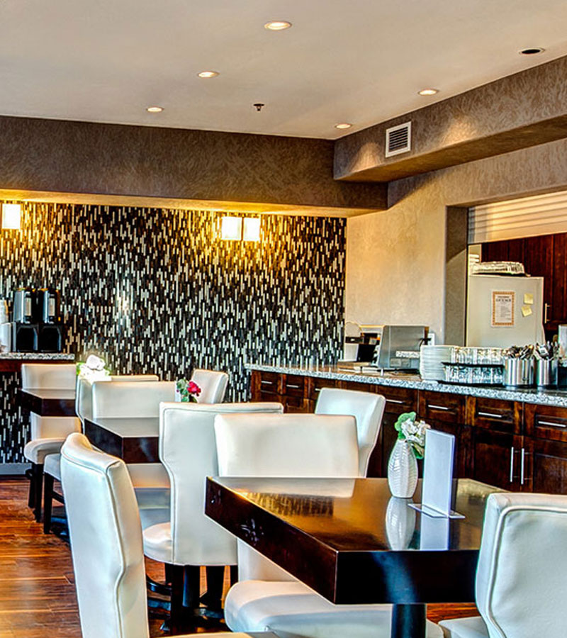 The breakfast area at d3h Home Inn & Suites Yorkton features hardwood flooring, a long wood paneled granite top breakfast bar, and a granite eat-in counter (serving as a coffee bar) built against the black and white pattern accent wall at the back of the dining space.