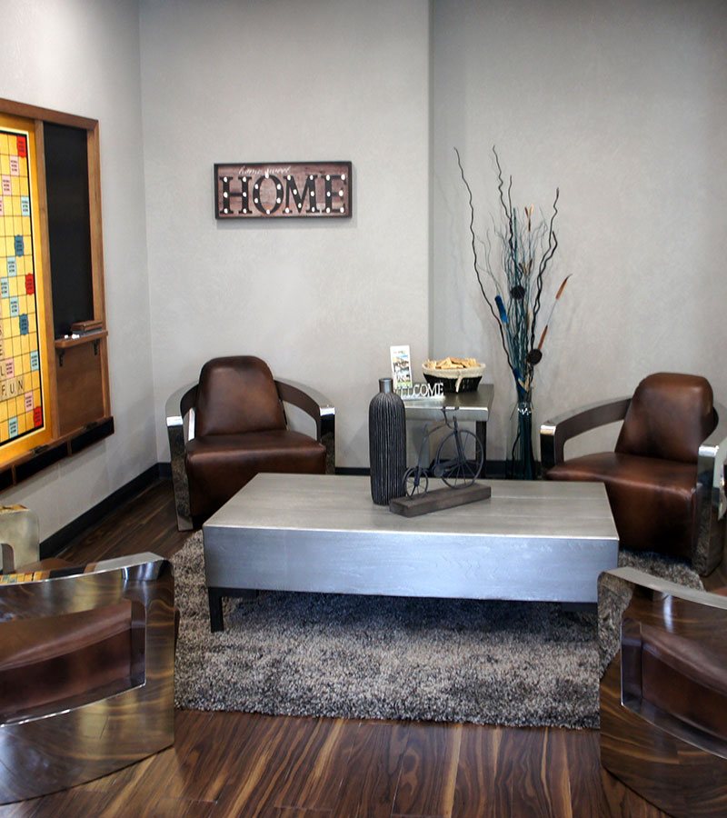 Four chocolate brown leather lounge chairs are placed around a heavy steel top coffee table embellished with decorative knick-knacks in the lounging area at the d3h Home Inn Express Medicine Hat hotel in Alberta.