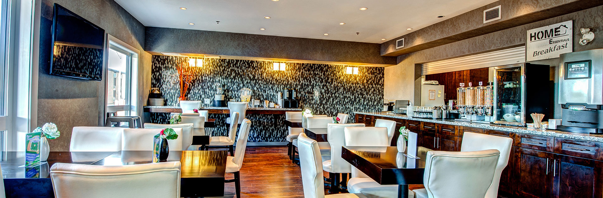 The breakfast area at d3h Home Inn & Suites Yorkton features hardwood flooring, a long wood paneled granite top breakfast bar, and a granite eat-in counter (serving as a coffee bar) built against the black and white pattern accent wall at the back of the dining space.